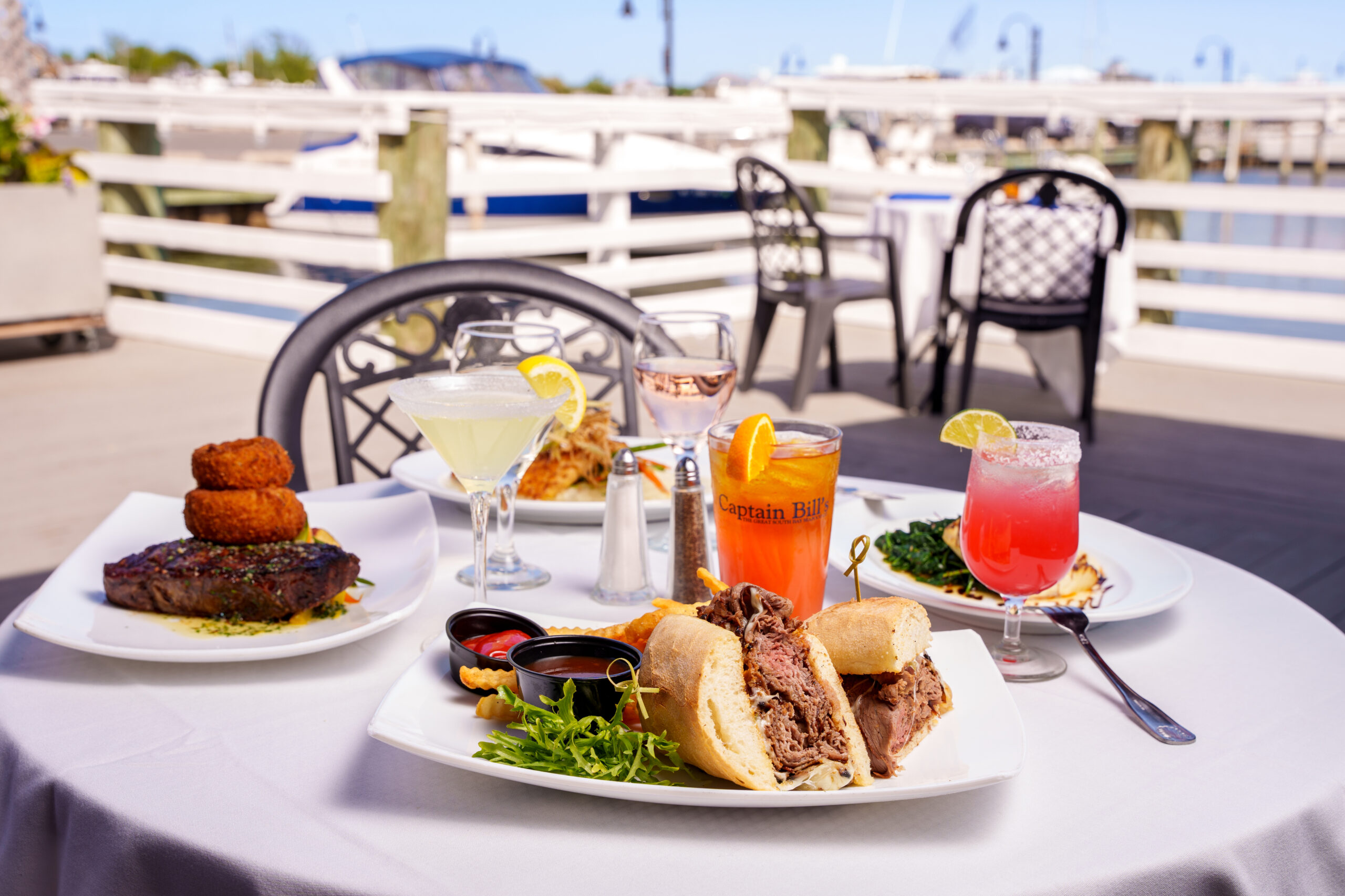 A table at an outdoor dining area near Shoregate Apartments in Bay Shore, featuring plates of food and cocktails.