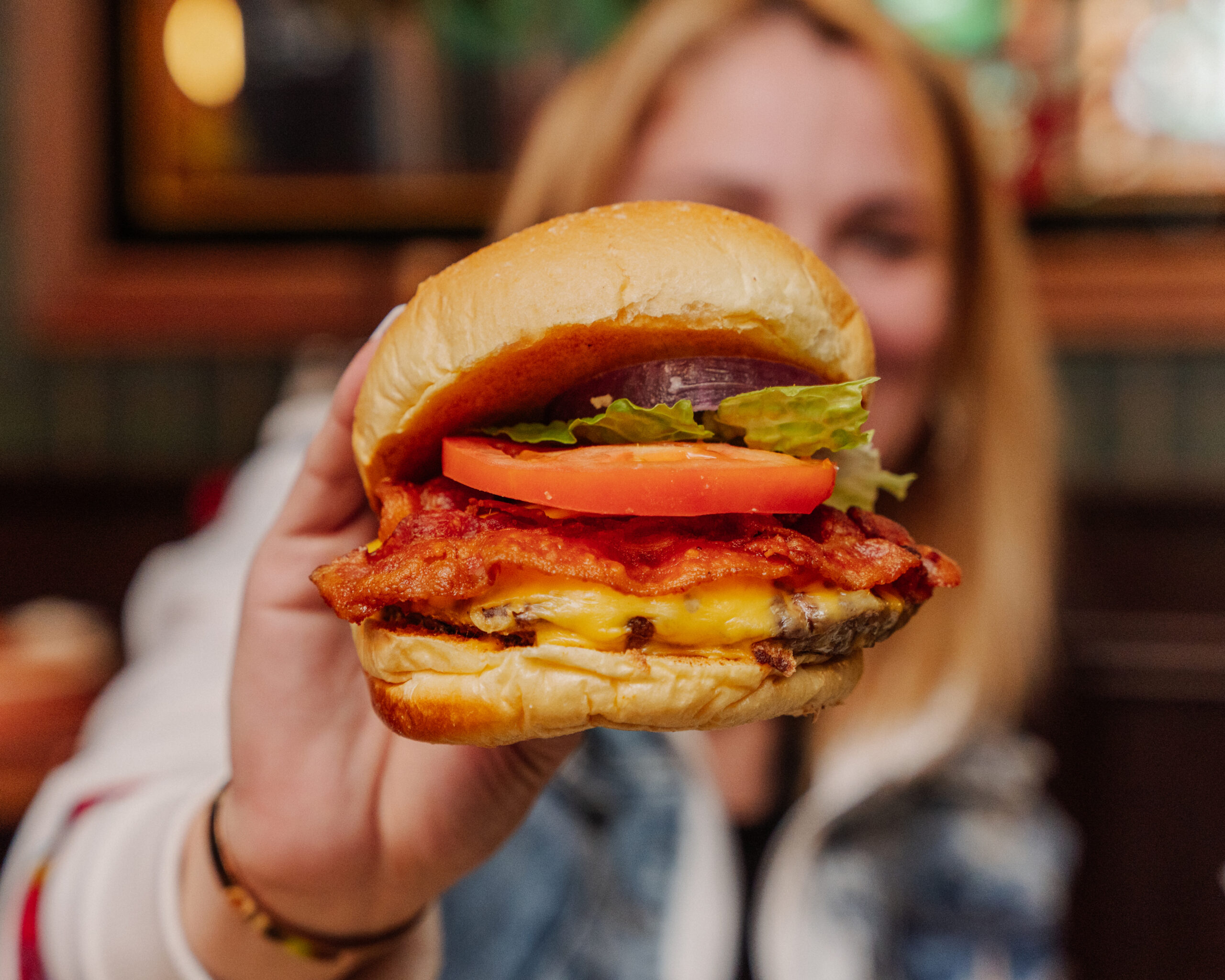 Someone holding up a burger at a restaurant near Shoregate Apartments in Bay Shore, featuring a woman in the background.
