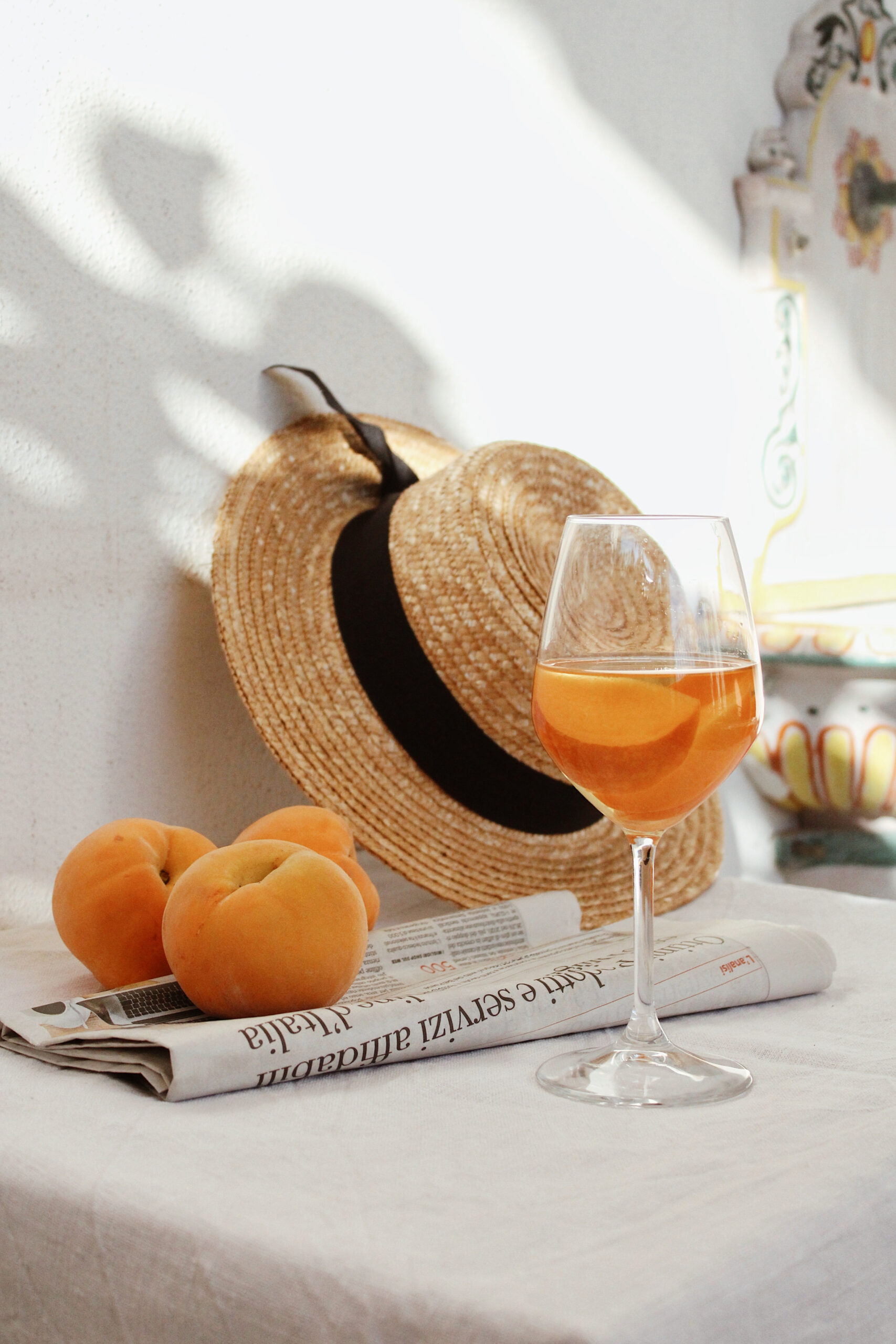A glass of wine with peaches and a sun hat at Shoregate Apartments in Bay Shore, featuring warm sunlight.